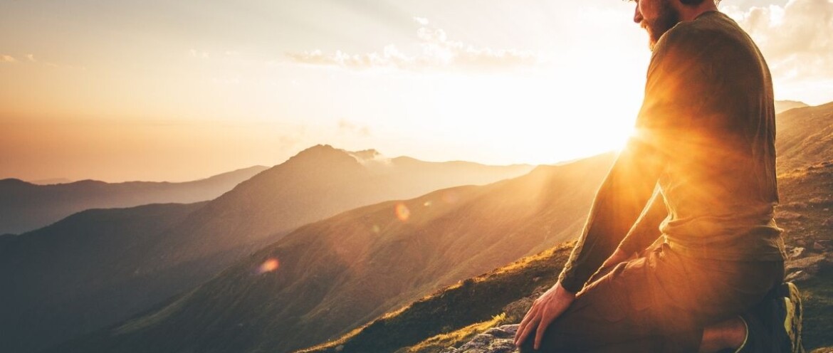 Mann kniet in der Abendsonne auf einem Berggipfel und blickt nach innen – ein Moment der Selbstbegegnung, Heilung und inneren Weite.