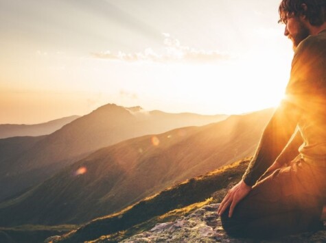 Mann kniet in der Abendsonne auf einem Berggipfel und blickt nach innen – ein Moment der Selbstbegegnung, Heilung und inneren Weite.