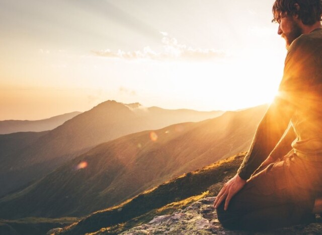 Mann kniet in der Abendsonne auf einem Berggipfel und blickt nach innen – ein Moment der Selbstbegegnung, Heilung und inneren Weite.