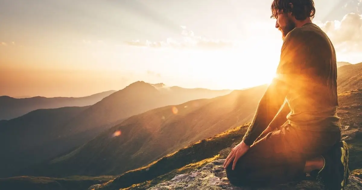 Mann kniet in der Abendsonne auf einem Berggipfel und blickt nach innen – ein Moment der Selbstbegegnung, Heilung und inneren Weite.